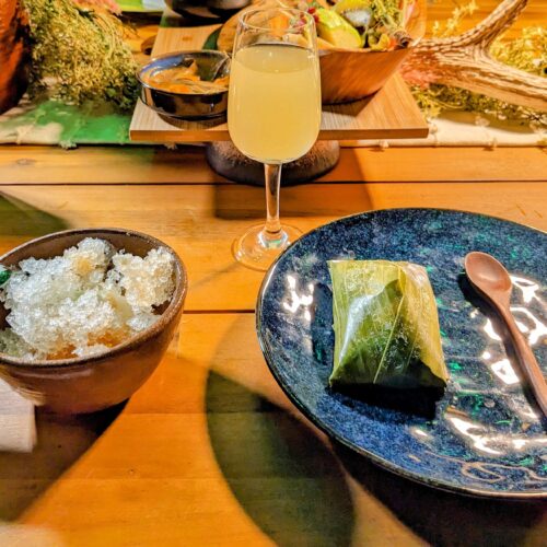 Two dessert plates and a glass of wine on a wooden table in an upscale restaurant.